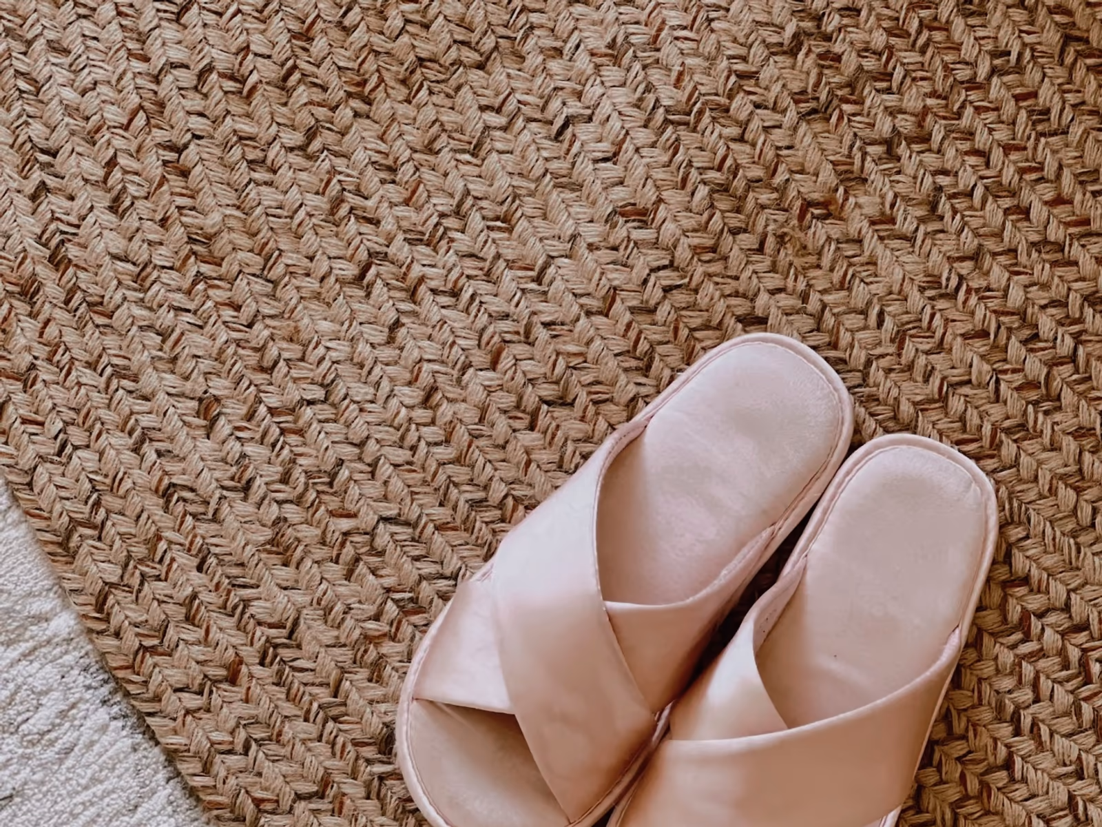 A pair of soft blush slippers resting on a woven jute rug