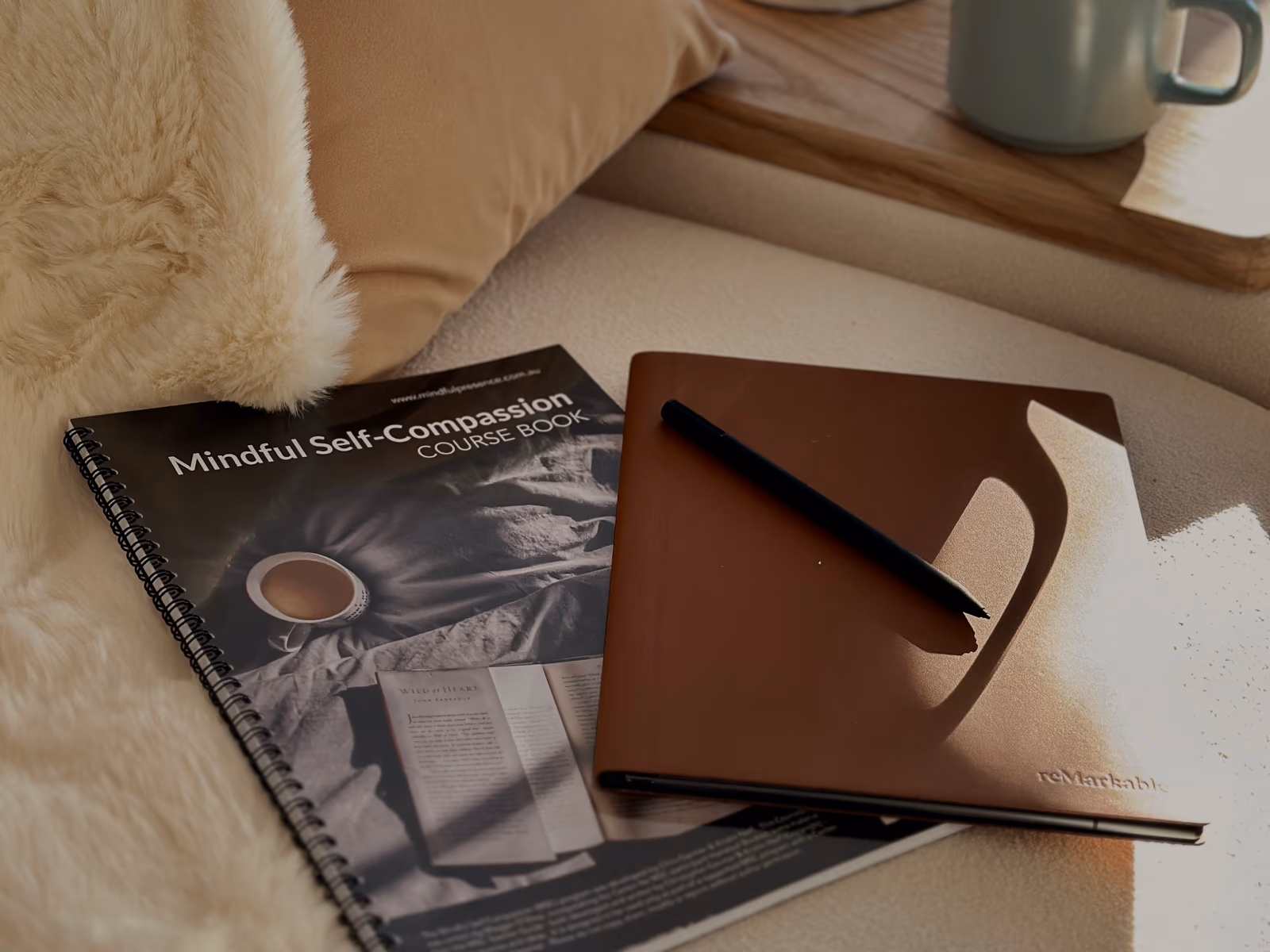 A mindful self-compassion workbook and journal resting on a soft sheepskin beside a sage mug