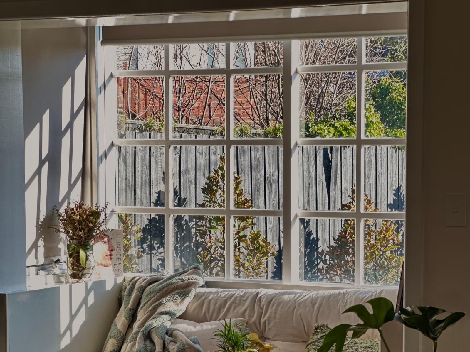 A cushioned window seat with a folded throw, bathed in afternoon light