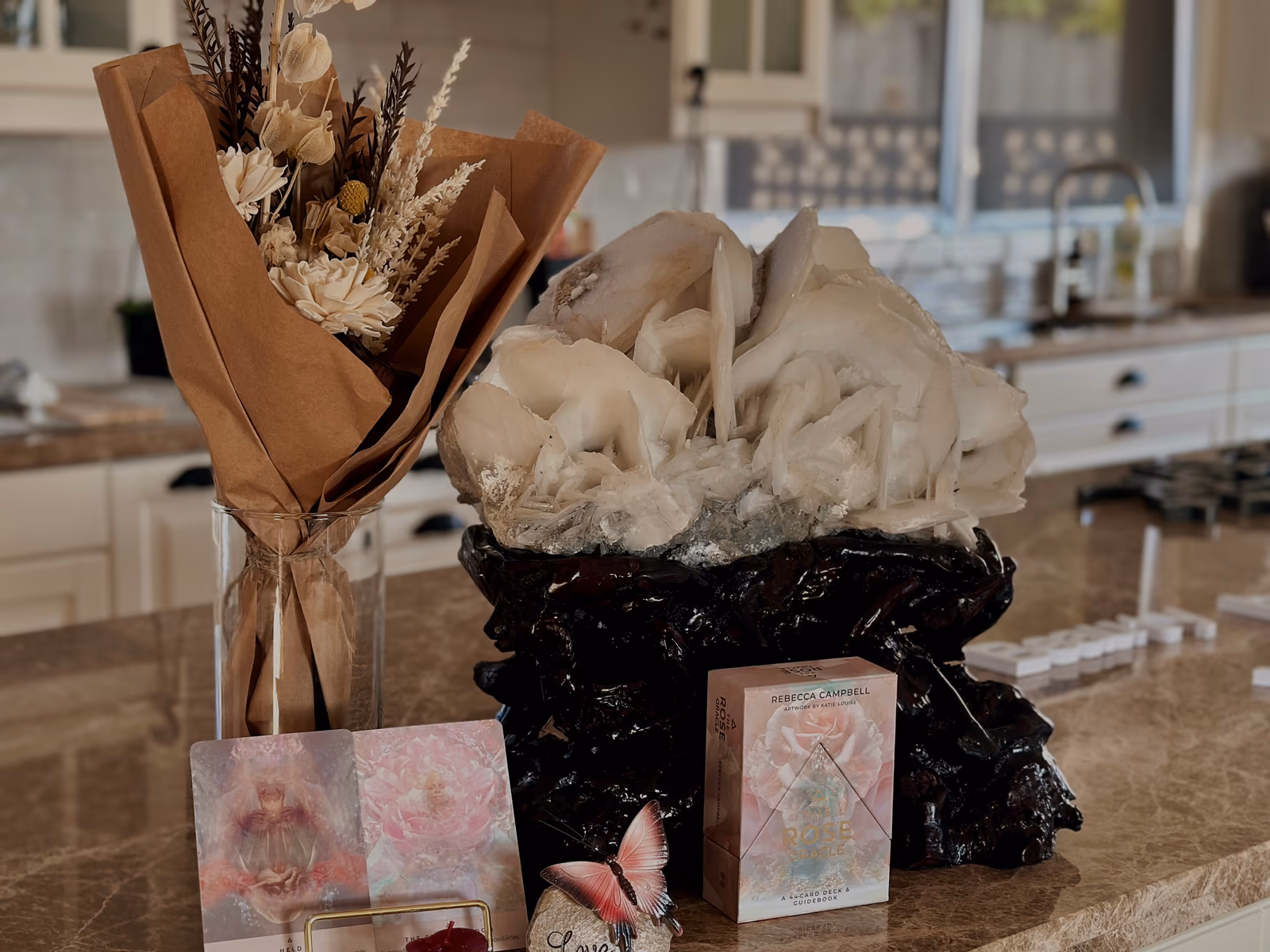 A dried-flower bouquet, a clear-quartz cluster, and an oracle deck on a stone bench