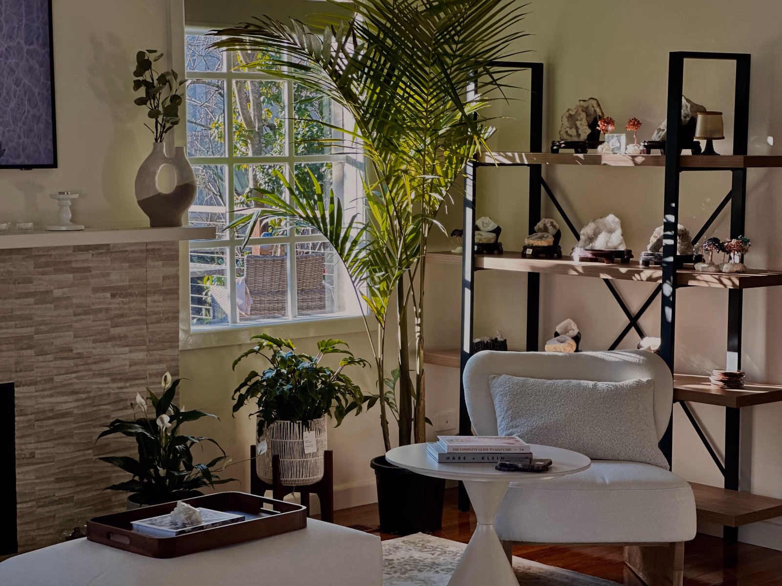 A calm corner with a boucle armchair, a sunlit window, and shelves of crystals